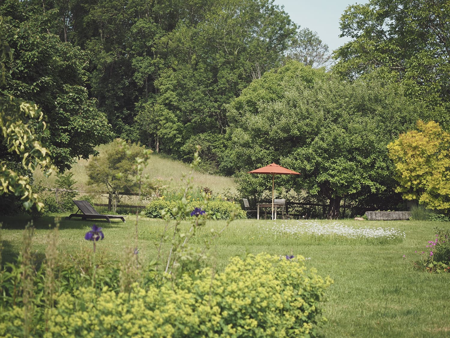 Blick auf einen Garten im Grünen mit Liegestuhl und Sonnenschirm